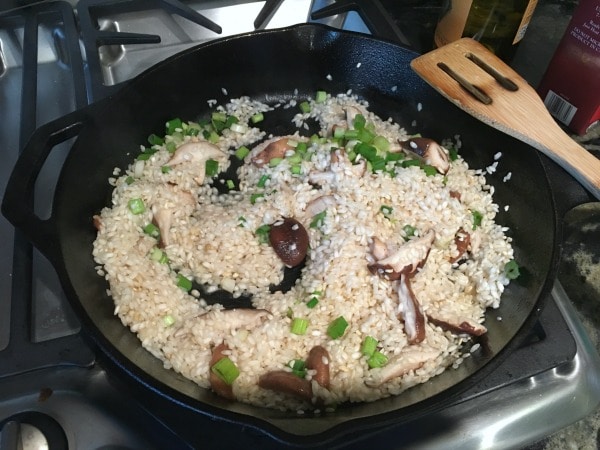 Adding shiitake mushrooms and scallions to cooking rice in a skillet
