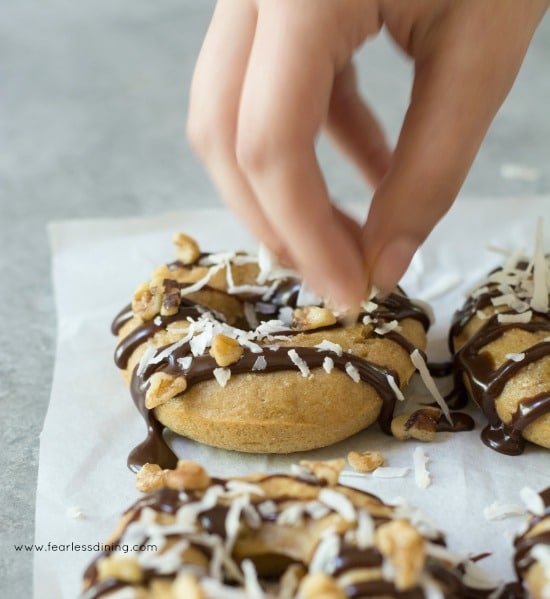 Fingers dropping walnuts onto Gluten Free Banana Donuts.