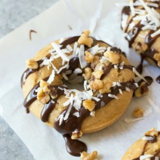 Gluten free banana donuts topped with chocolate, shredded coconut, and chopped walnuts.