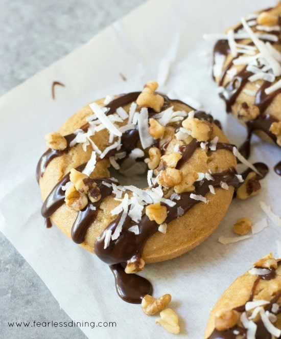 Gluten free banana donuts topped with chocolate, shredded coconut, and chopped walnuts.