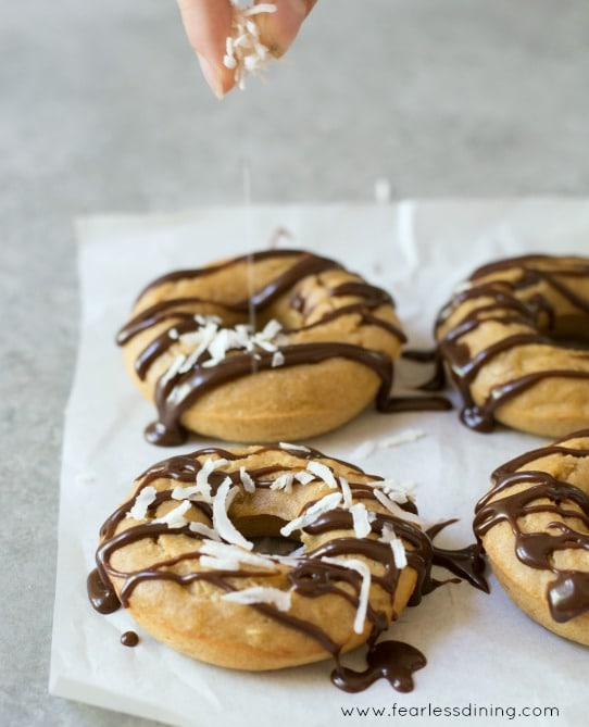 Fingers are dropping shredded coconut on to Gluten Free Banana Donuts.