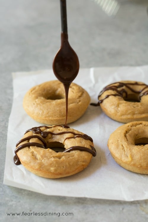 A spoon is drizzling chocolate onto Gluten free banana donuts.