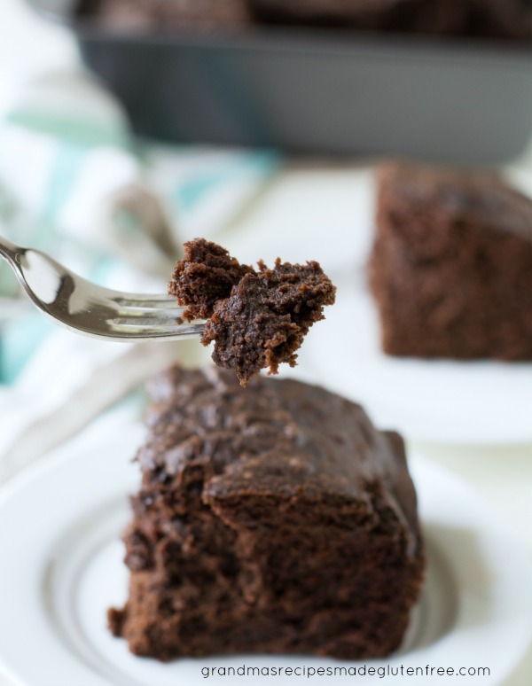 Gluten Free Devil's Food Cake slice on a plate. A fork is holding a bite of cake.