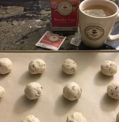 cookie dough balls on a cookie sheet and a cup of tea in the background