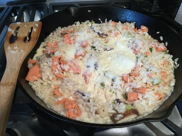 Adding smoked salmon and parmesean cheese to the risotto in a skillet.