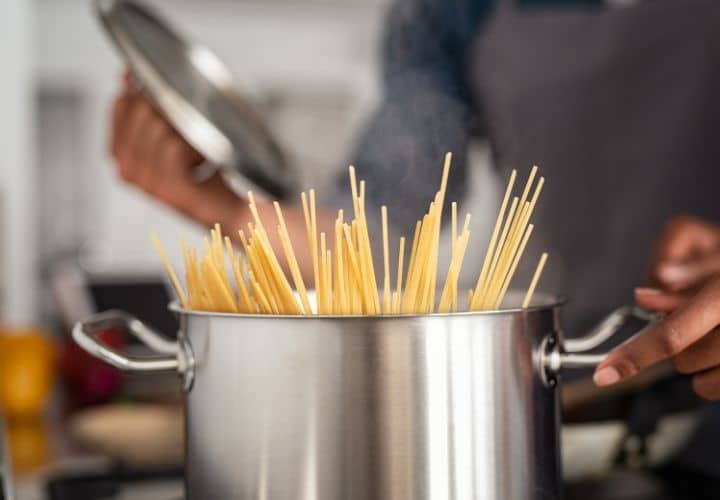 A tall silver pot that is cooking spaghetti. The spaghetti is cooking down so uncooked spaghetti is sticking up out of the pot.