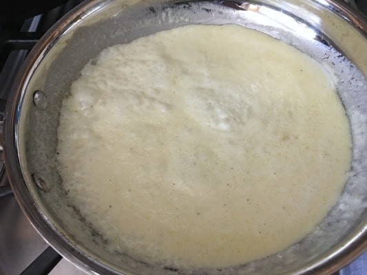 The Alfredo sauce simmering in a pan.
