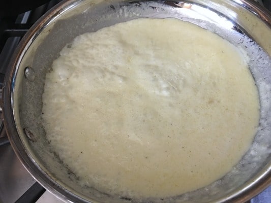 The Alfredo sauce simmering in a pan.
