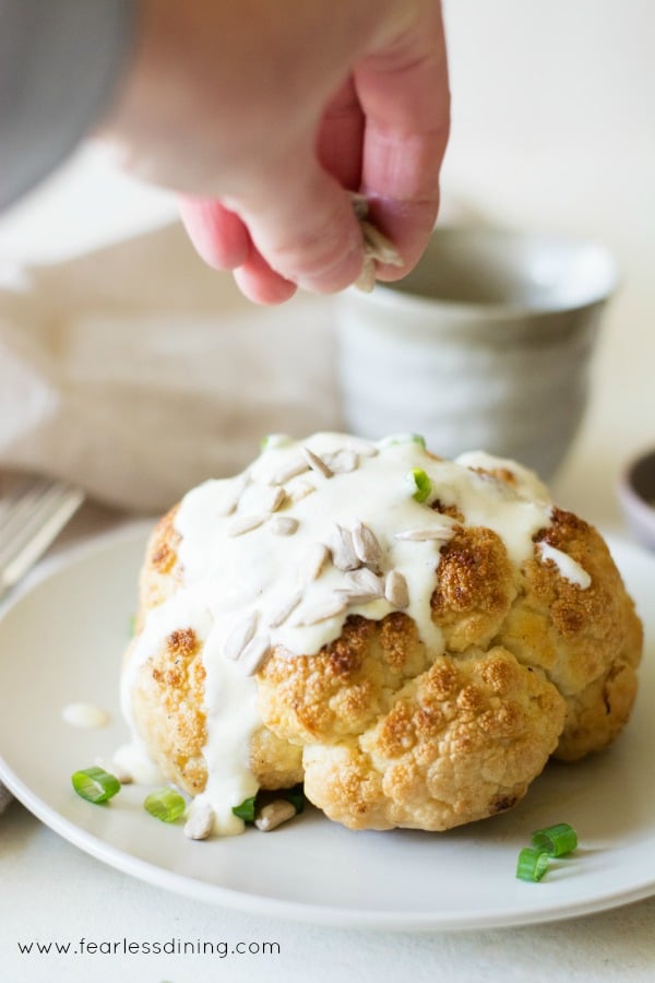 A hand sprinkling sunflower seeds on a roasted whole cauliflower.