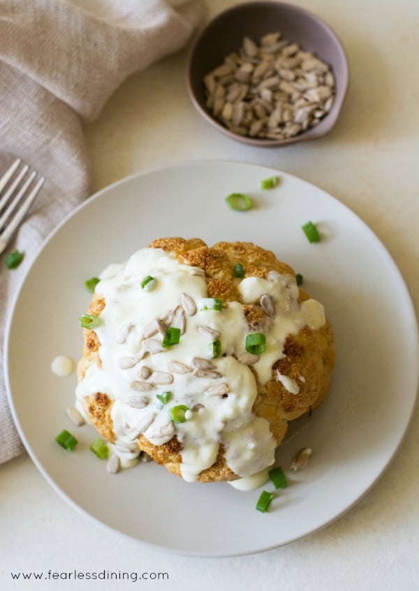 Top view of a whole roasted cauliflower topped with alfredo sauce.