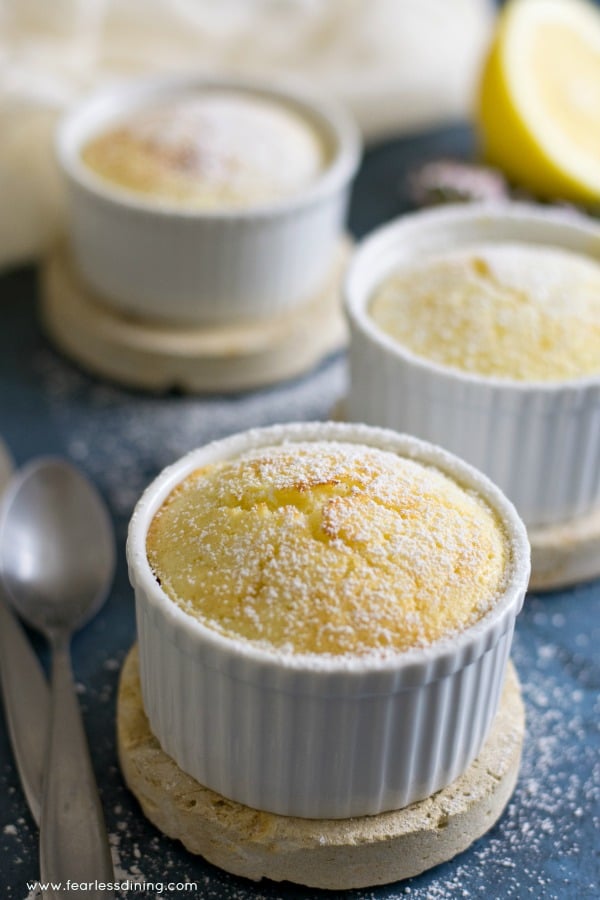 Gluten Free Lemon Sour Cream Souffle Cakes in a row. Spoons are on the side of the ramekin.