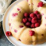 overhead image of a gluten free vanilla bundt cake with raspberries, sitting on a cake plate. The center of the bundt is filled with fresh berries