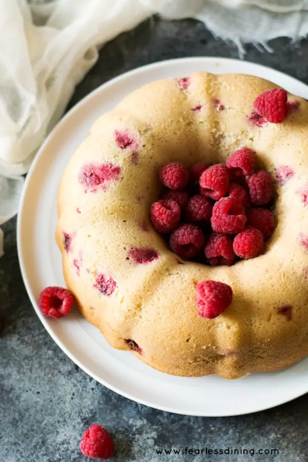 overhead image of a gluten free vanilla bundt cake with raspberries, sitting on a cake plate. The center of the bundt is filled with fresh berries