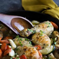 Chicken legs in a pot being stirred with a wooden spoon.