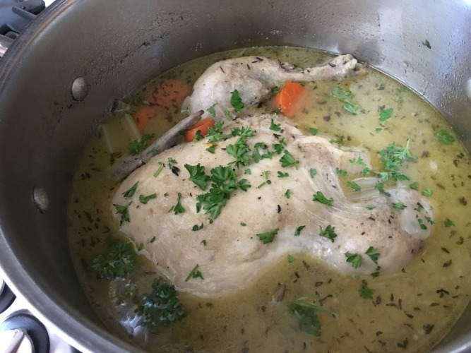 The chicken cooking in soup with parsley and carrots.