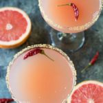 overhead photo of 2 glasses of pink grapefruit margaritas with red chile peppers floating in them.