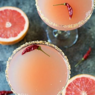 overhead photo of 2 glasses of pink grapefruit margaritas with red chile peppers floating in them.