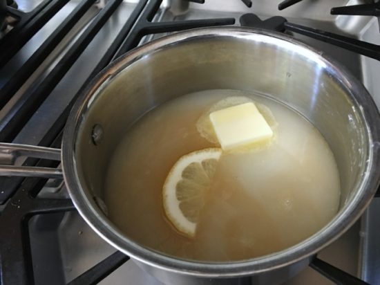 Adding butter and lemon to the pot of cream sauce ingredients.