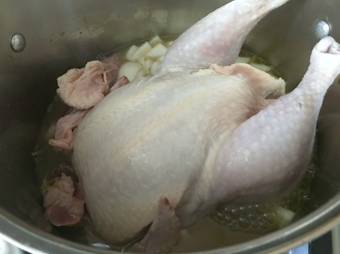 A whole chicken cooking in a soup pot.