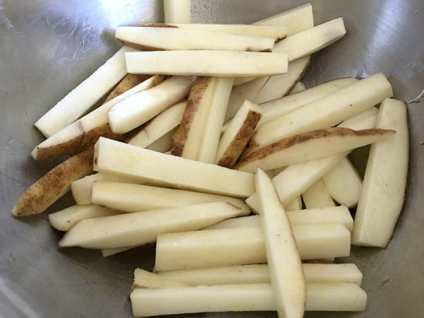 Raw potatoes cut lengthwise in a bowl.