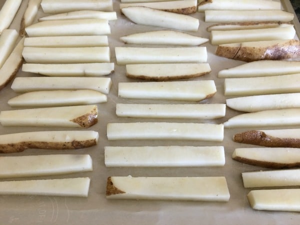 Raw potato wedges lined up on a baking sheet.