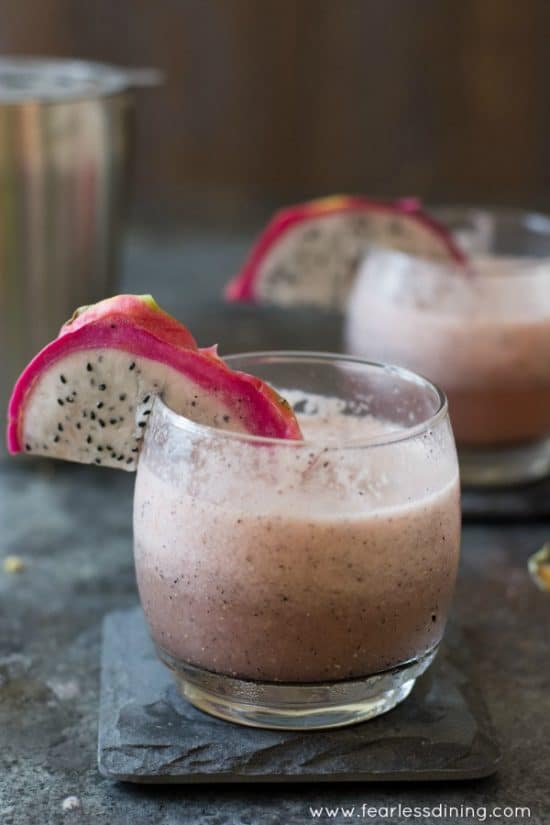 a glass of pink dragon fruit cocktail with vodka. The glass is garnished with a slice of fresh dragon fruit