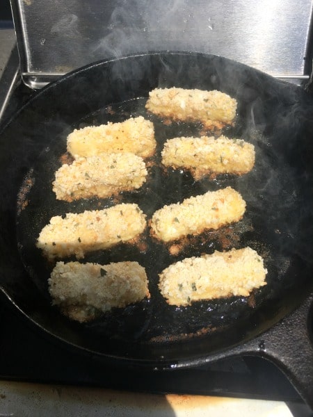 Frying cheese sticks in hot oil in a cast iron skillet.