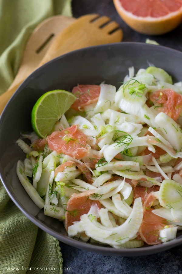 A large bowl of pink grapefruit and fennel salad. Salad tongs are along the side of the bowl.