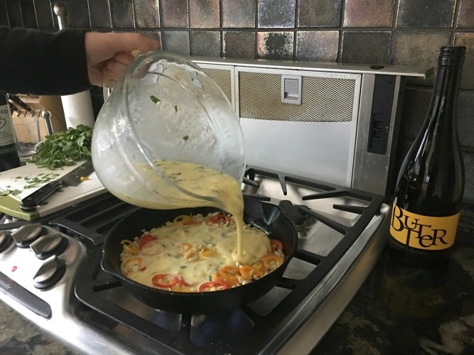 Pouring the egg mixture into the skillet with the vegetables.