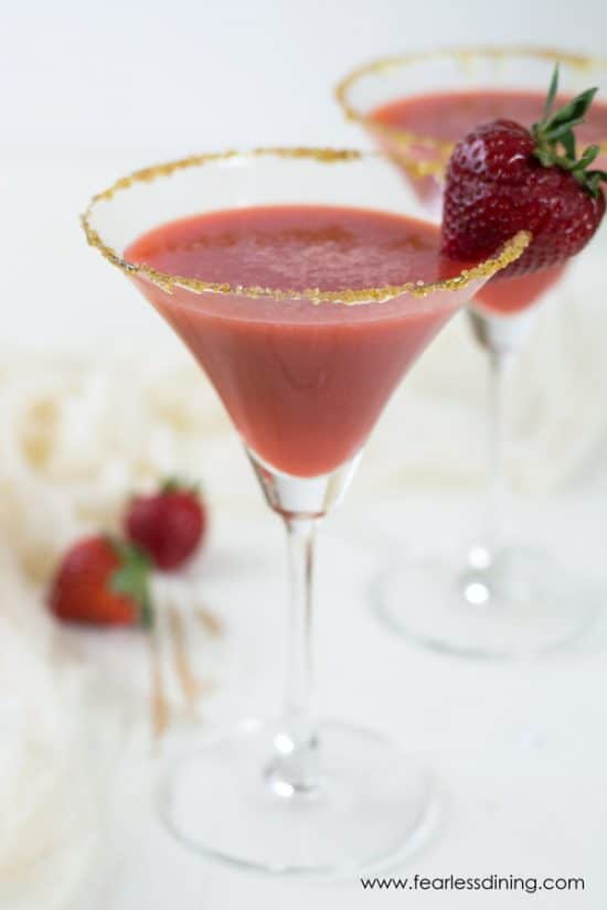 Martini glasses filled with honey gin strawberry ginger cocktails. The glasses have fresh strawberry garnishes.