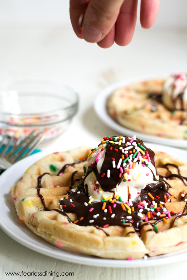A hand is dropping colorful sprinkles on top of a cake batter Waffle Sunday.