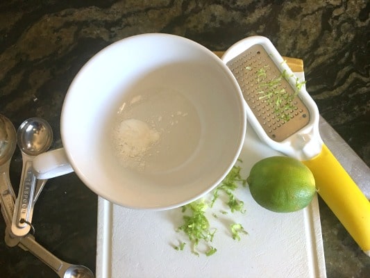 A mug with baking powder and lots of lime zest on a cutting board.