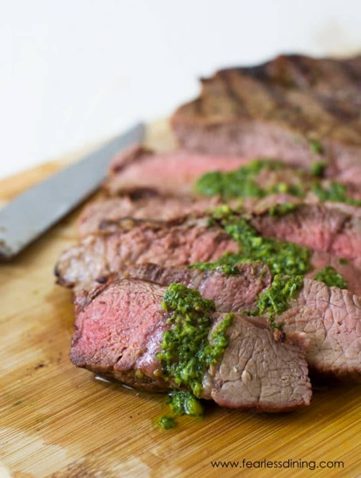 A sliced NY strip steak on a cutting board topped with basil garlic sauce.