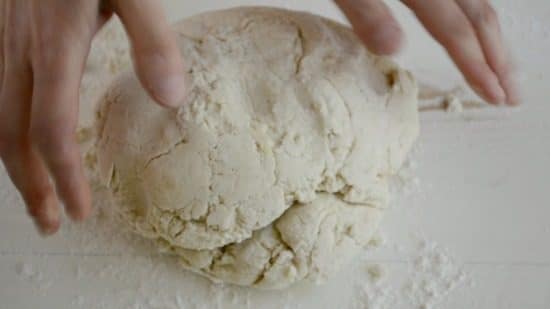 Hands shaping pizza dough on a counter.
