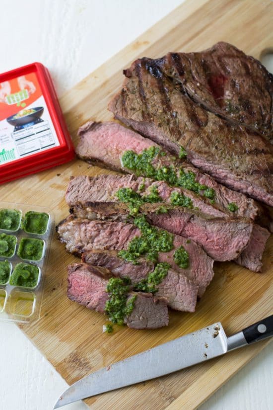 Steak on a cutting board with a basil sauce on top.