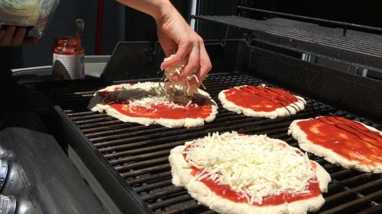 Four personal sized pizzas cooking on a grill.