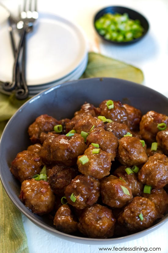A bowl of barbecue turkey meatballs with plates in the background