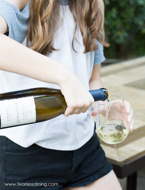 A woman pouring white wine into a stemless wine glass she is holding.