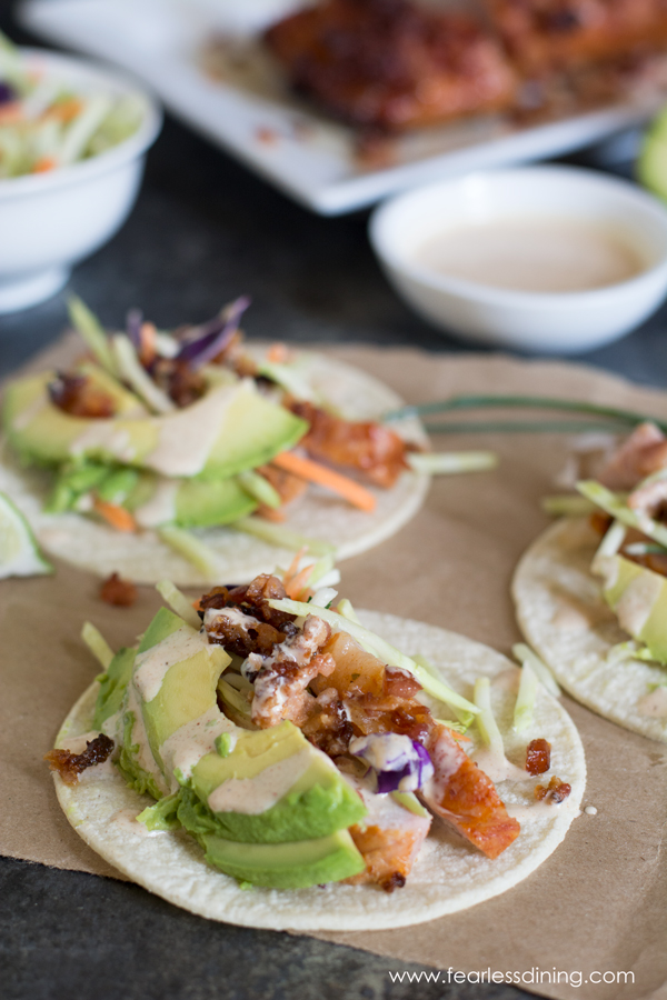 Grilled pork tenderloin street tacos on a paper bag. The tacos are topped with avocado and a chipotle sauce.