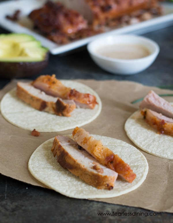 Sliced pork tenderloin on small corn tortillas. There is a small bowl of sauce behind the tacos.