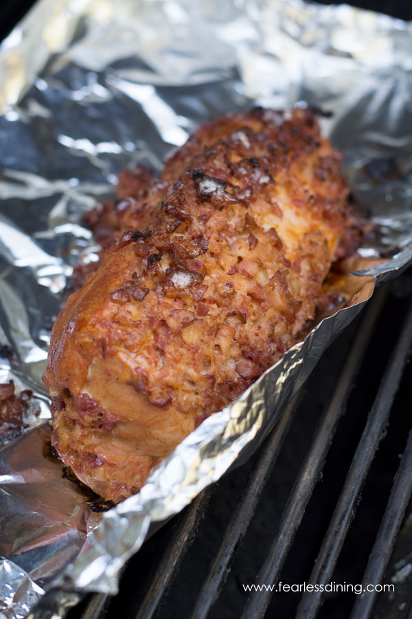 A piece of foil with the cooked tenderloin on top of it. The foil is on the grill.