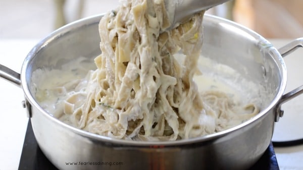 Tongs holding up a serving of fettuccine alfredo.