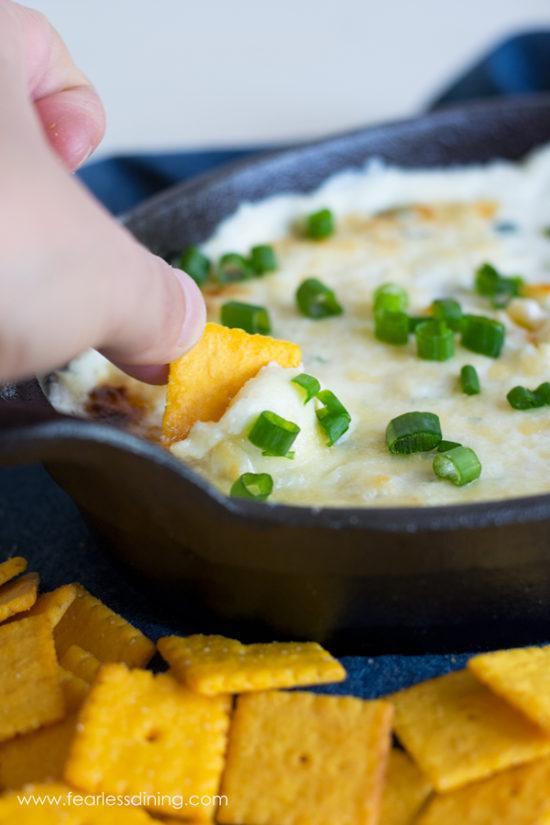 A cracker dipping into the gooey cheese.