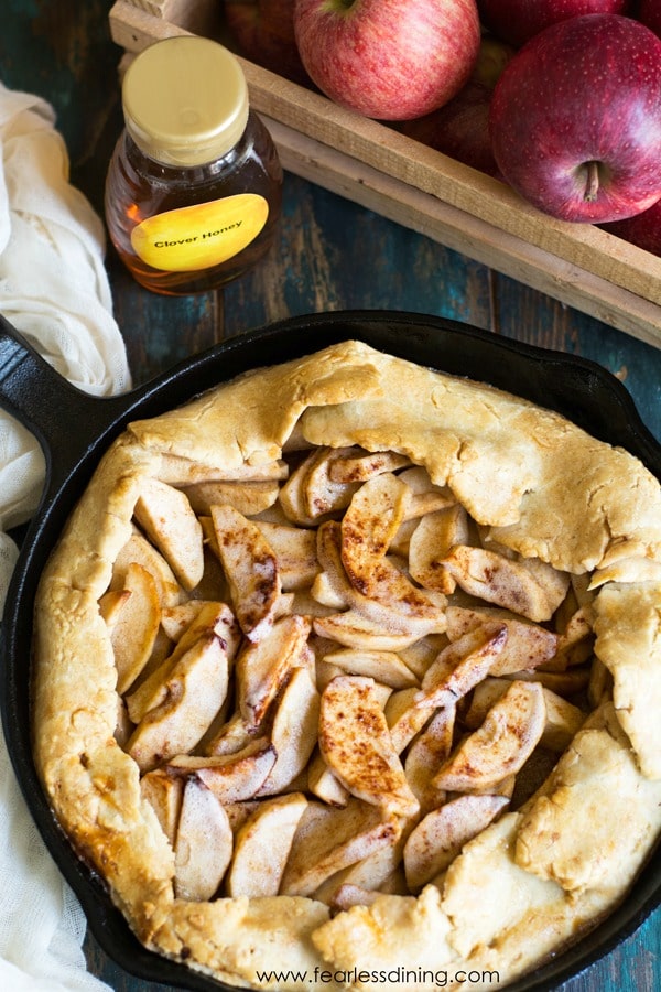 top view of a gluten free galette with apples and honey - a bottle of honey and fresh red apples next to it.