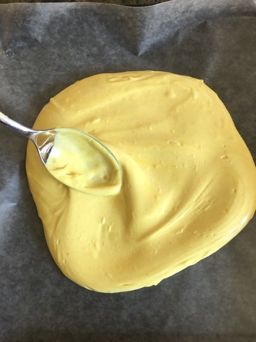 Melted turmeric candy being spread on a piece of wax paper.