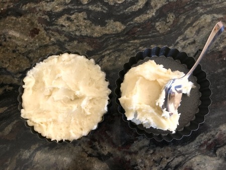 Adding mashed potatoes to round tart pans.