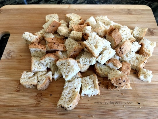 Cubed gluten free bread on a wooden cutting board.