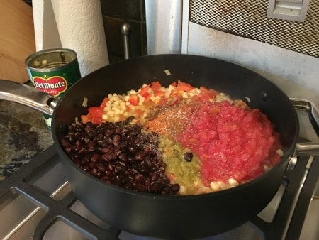 Corn, onion, diced tomatoes and black beans cooking on the stove.