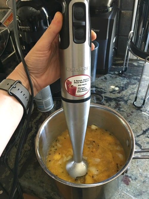 An immersion blender is in the pot pureeing all of the ingredients