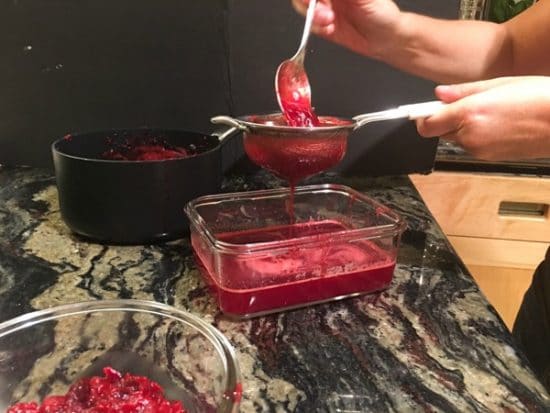 Pressing the cooked cranberry mixture through a strainer.